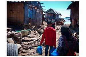 A photo of two people carrying bags, walking around village houses