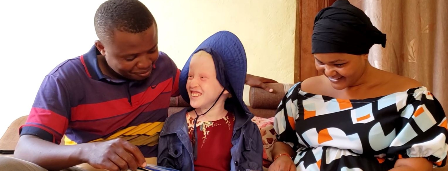 A photo of Francis, Joyce and Edith looking at a book together. Photo Credits: Visual Journey team “TUNAWEZA_Raising Awareness About Albinism”